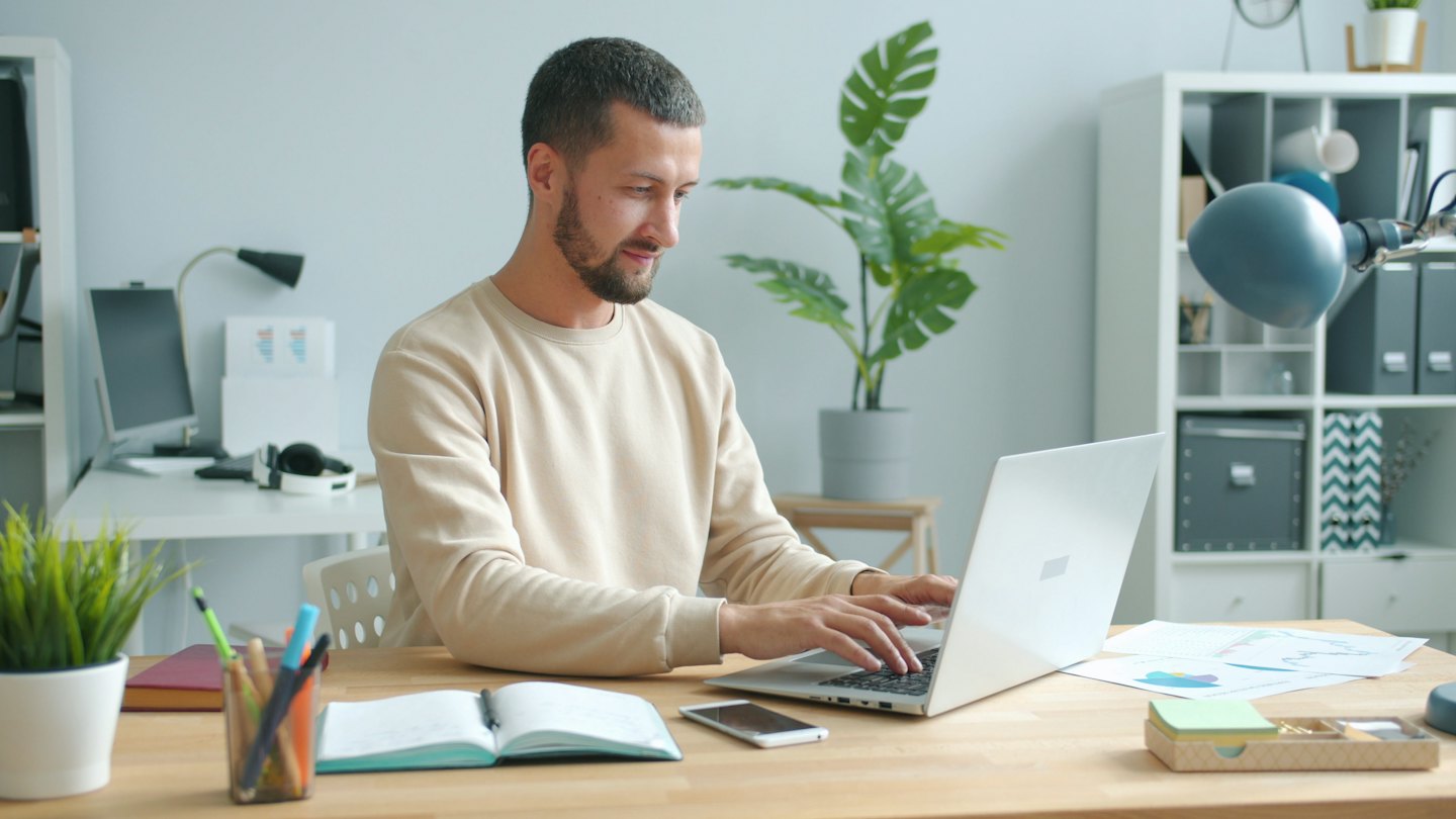 A man works on his laptop at a tidy wooden desk.